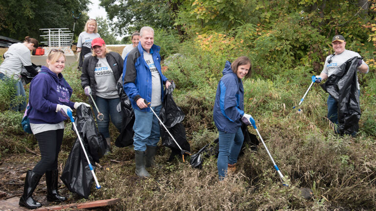 Watts employees completing Merrimack river clean up with poles and bags.